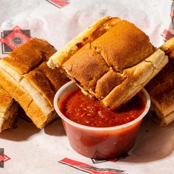 Toasted breadsticks with a side of marinara sauce in a paper-lined basket.